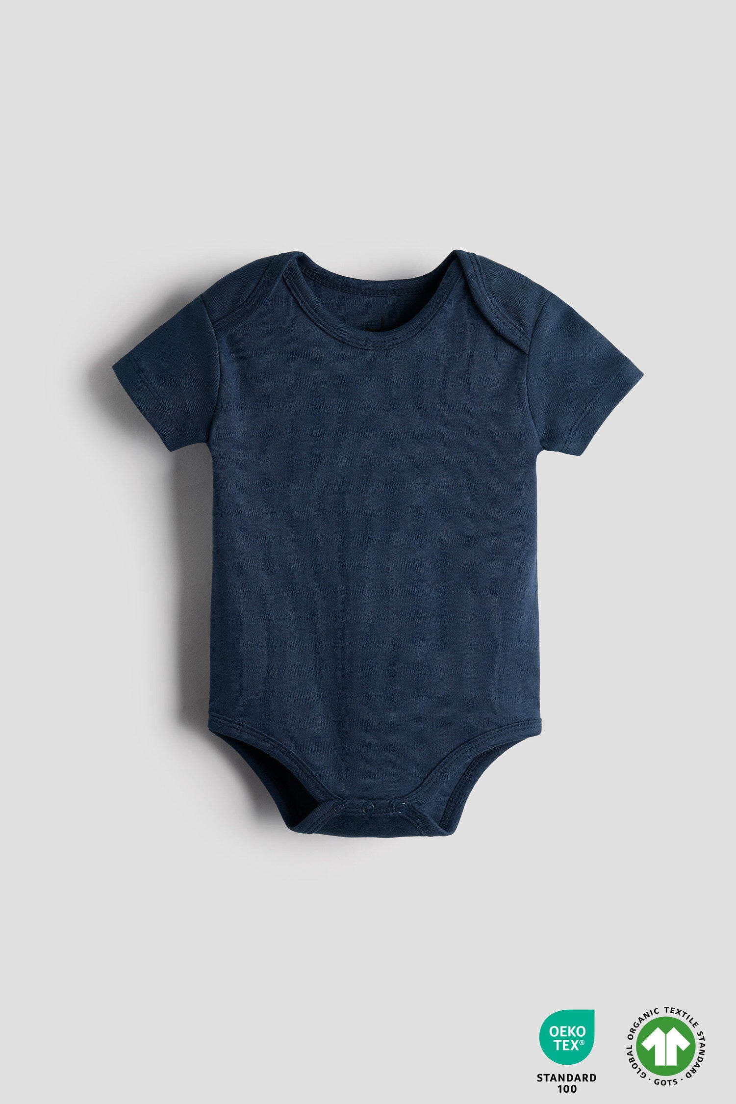 Navy blue baby bodysuit on a light gray background with OEKO-TEX and GOTS labels.