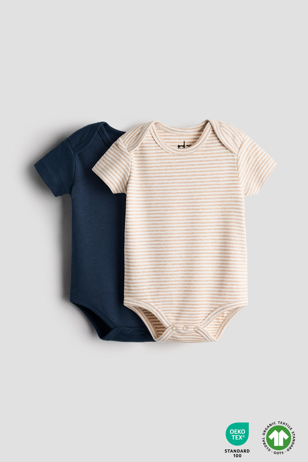 Two baby bodysuits, one navy and one beige with white stripes, on a light gray background.