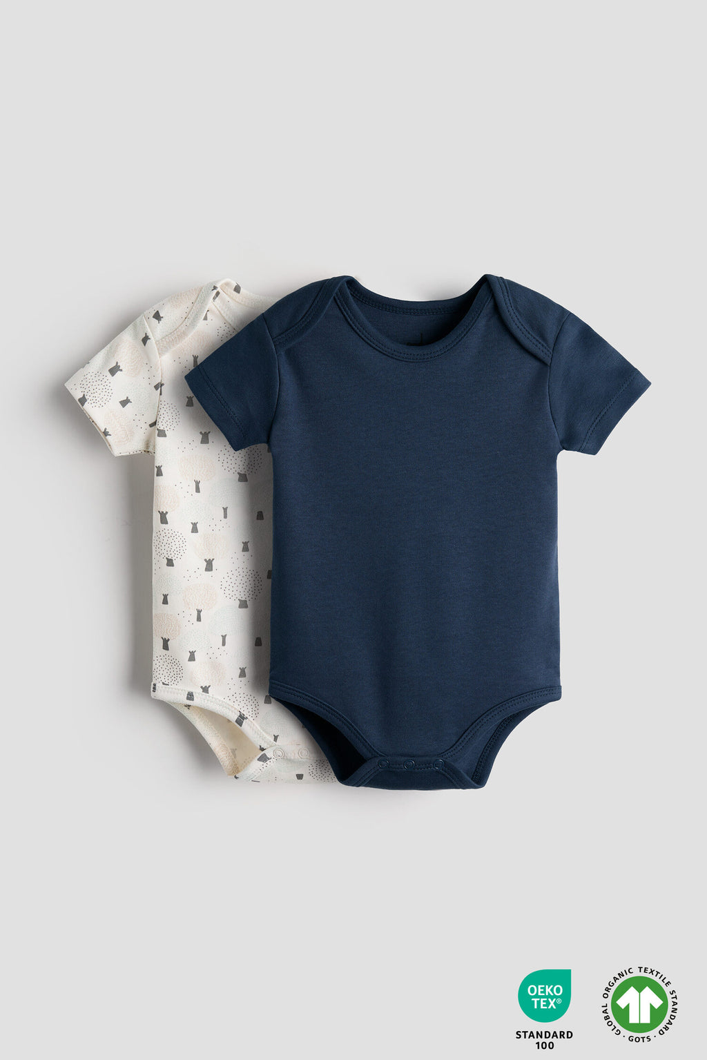 Navy blue baby bodysuit and patterned baby blanket on a light gray background with OEKO-TEX and Global Organic Textile Standards logos.