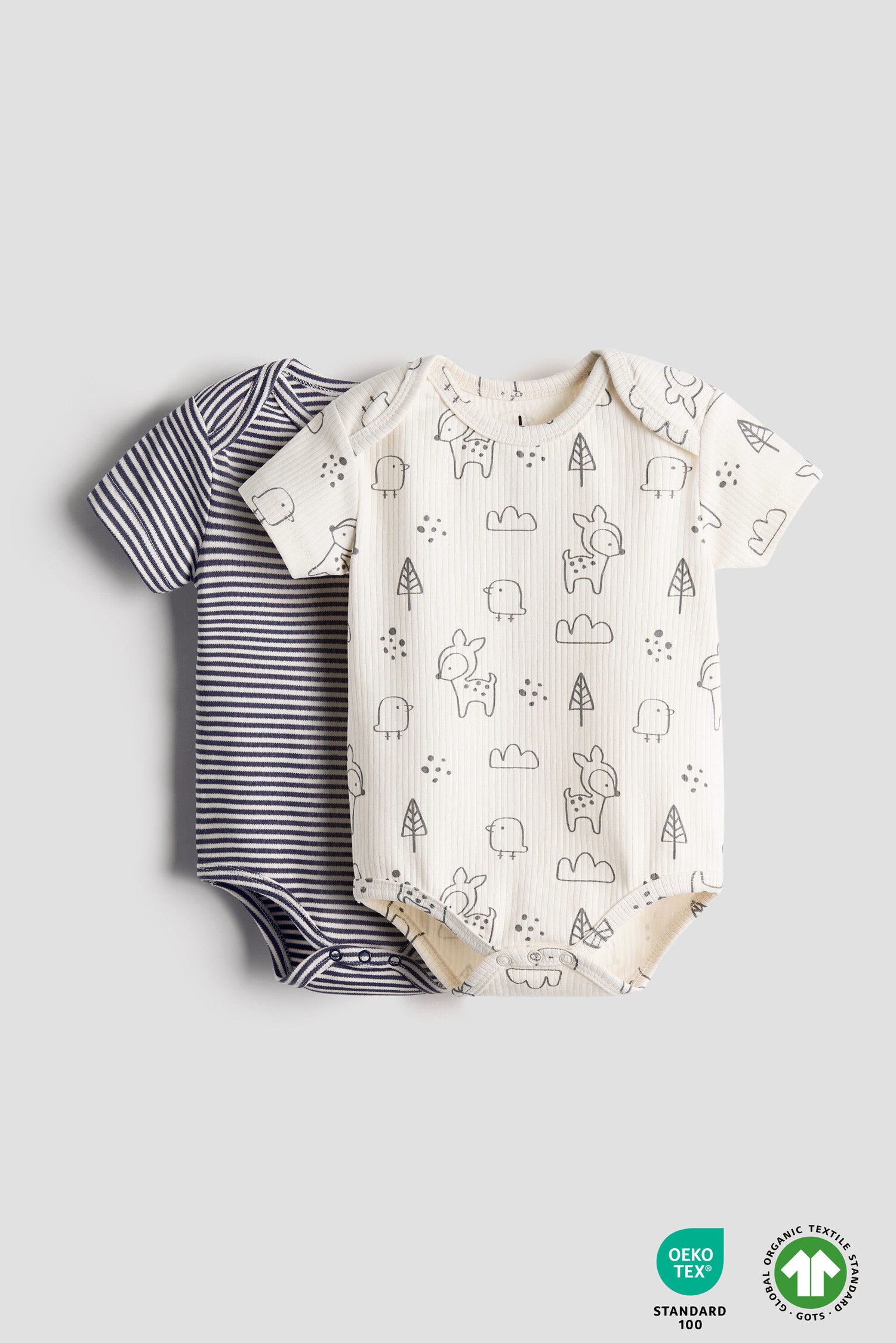 Two baby bodysuits, one striped and one with a forest pattern, on a light gray background.