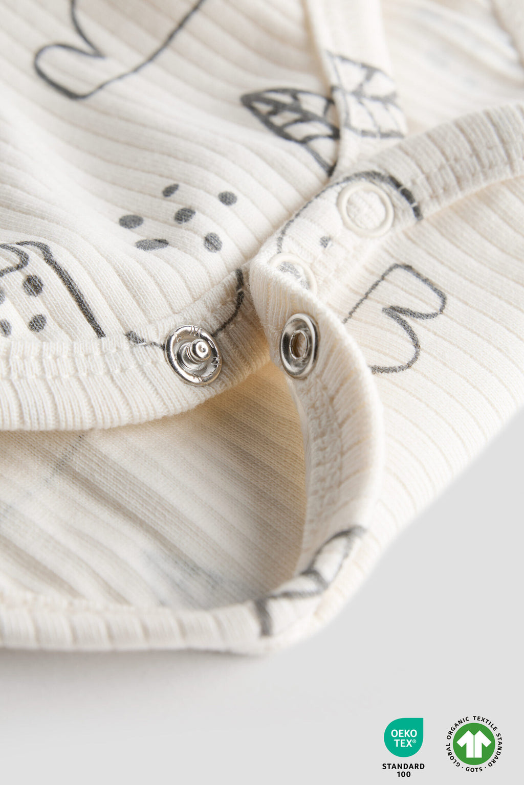 Close-up of a baby romper with butterfly patterns and buttons on a light background.