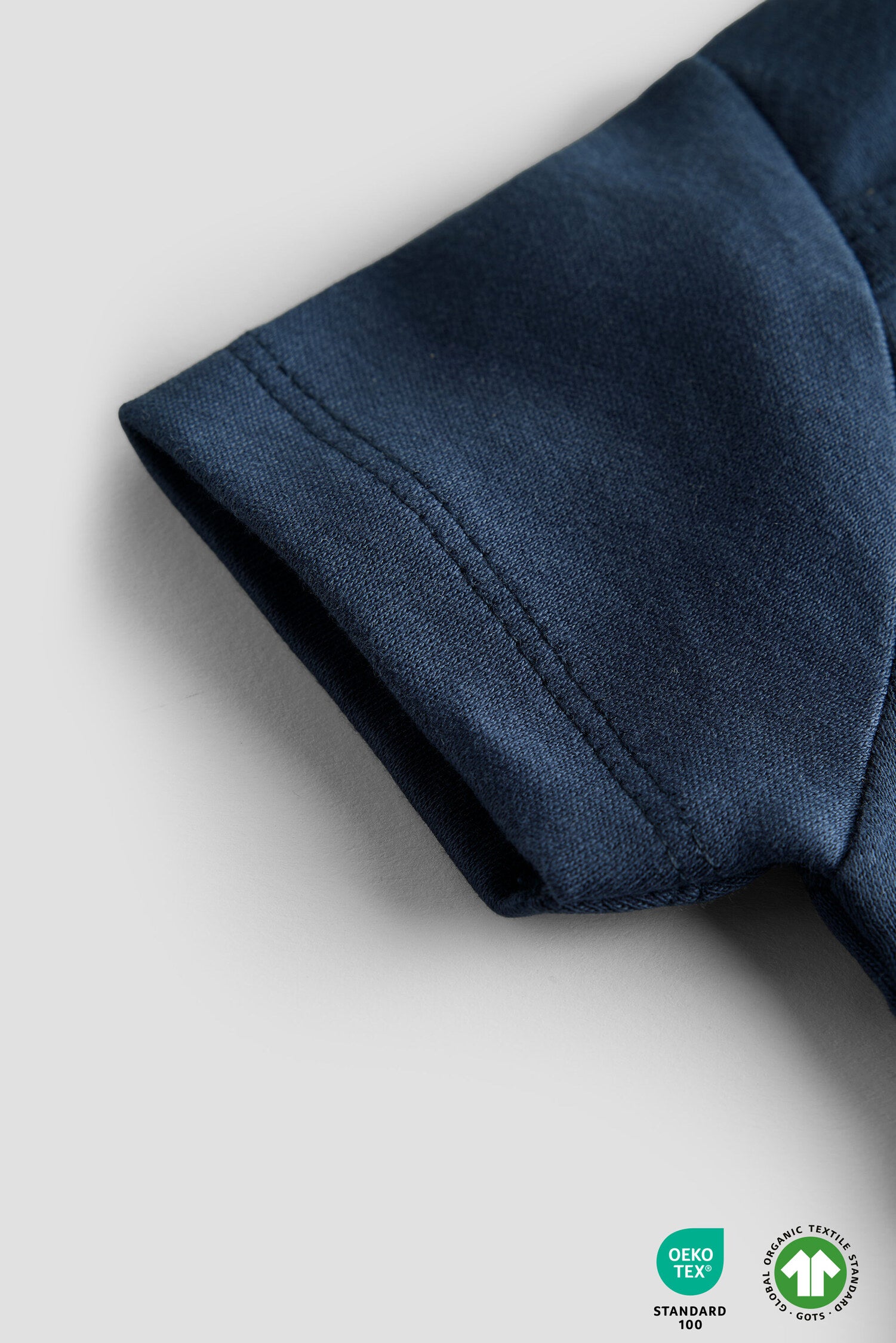 Close-up of a navy blue fabric sleeve on a light gray background with OEKO-TEX and GOTS logos.