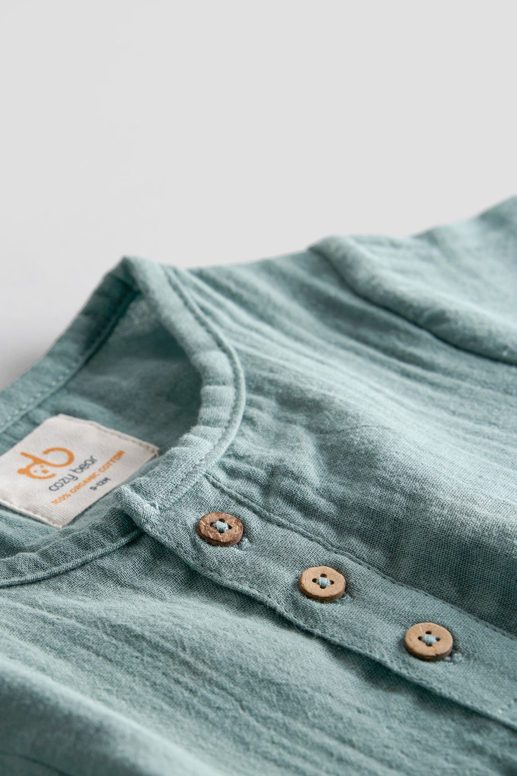 Close-up of a light blue shirt with buttons and a brand label on a gray background