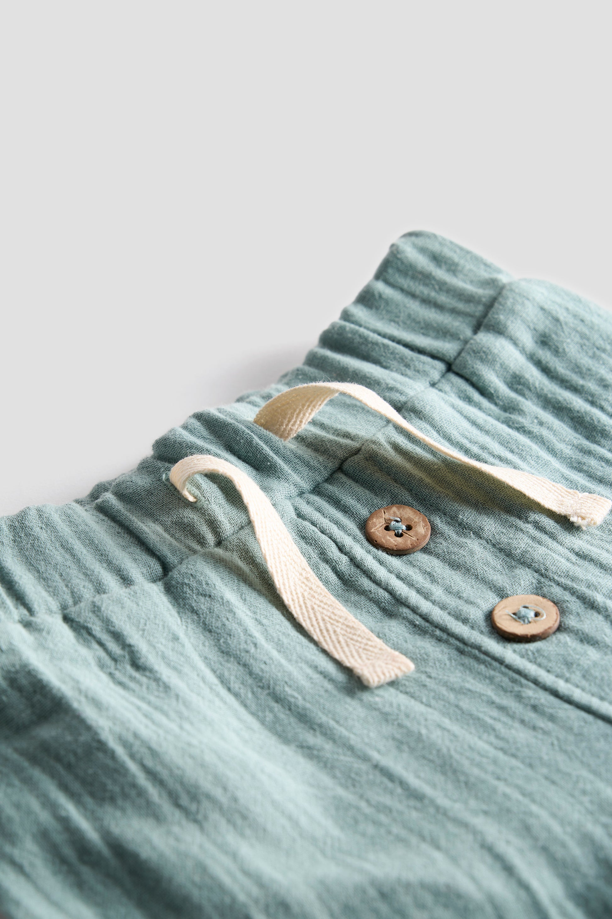 Light blue velour shorts with a drawstring and buttons on a light gray background