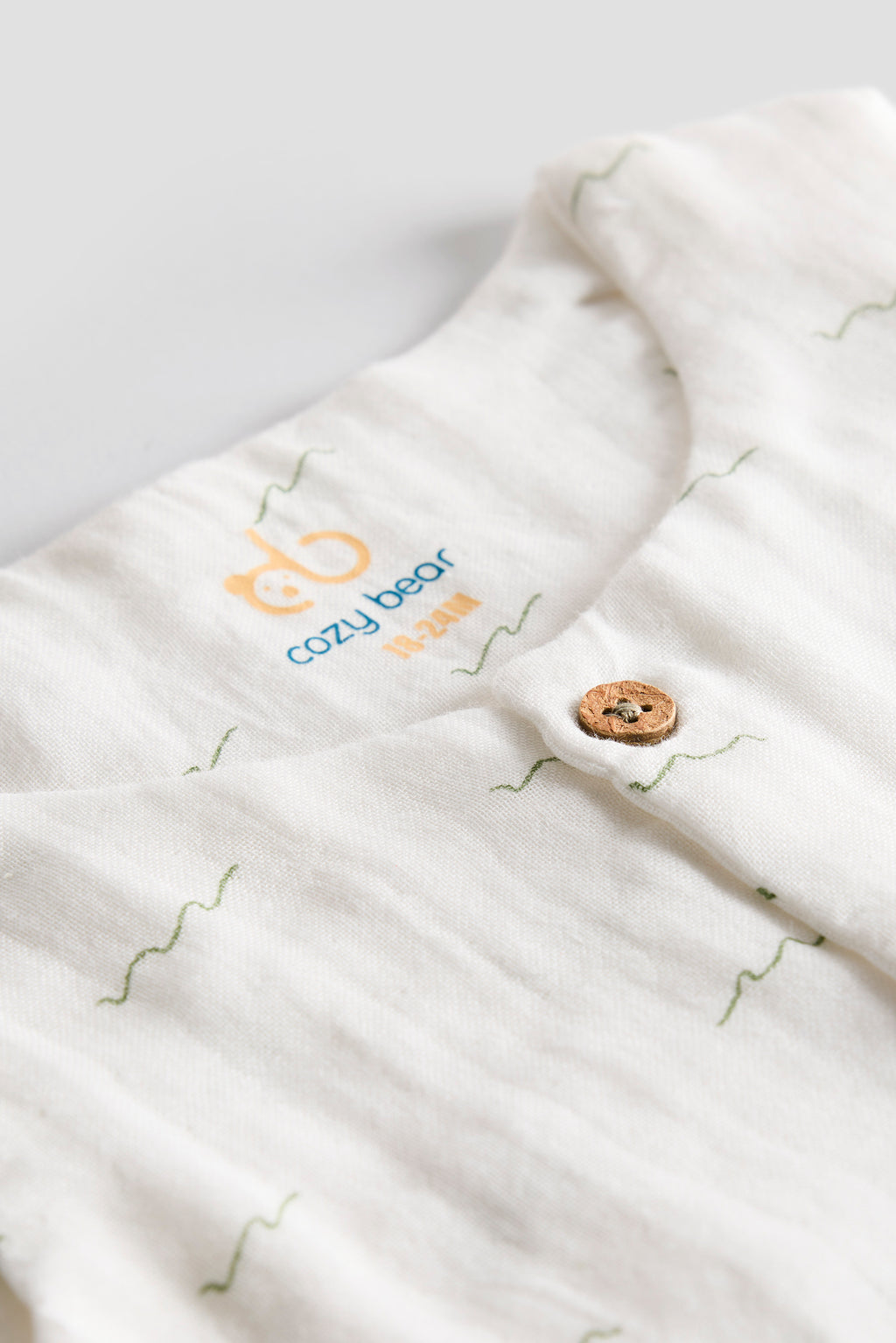 Close-up of a white baby swaddle with 'Cozy Bear' branding on a light gray background