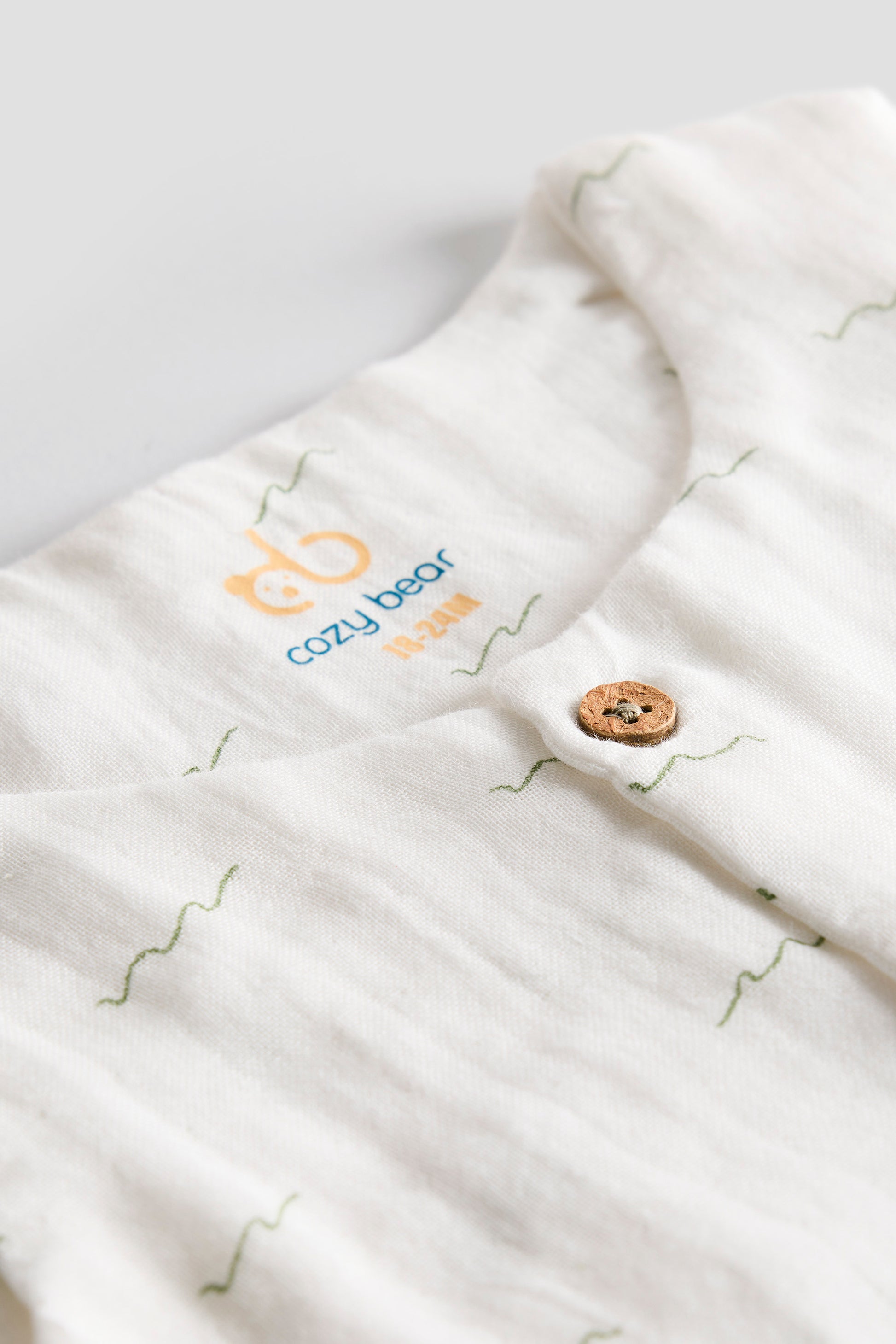 Close-up of a white baby swaddle with 'Cozy Bear' branding on a light gray background