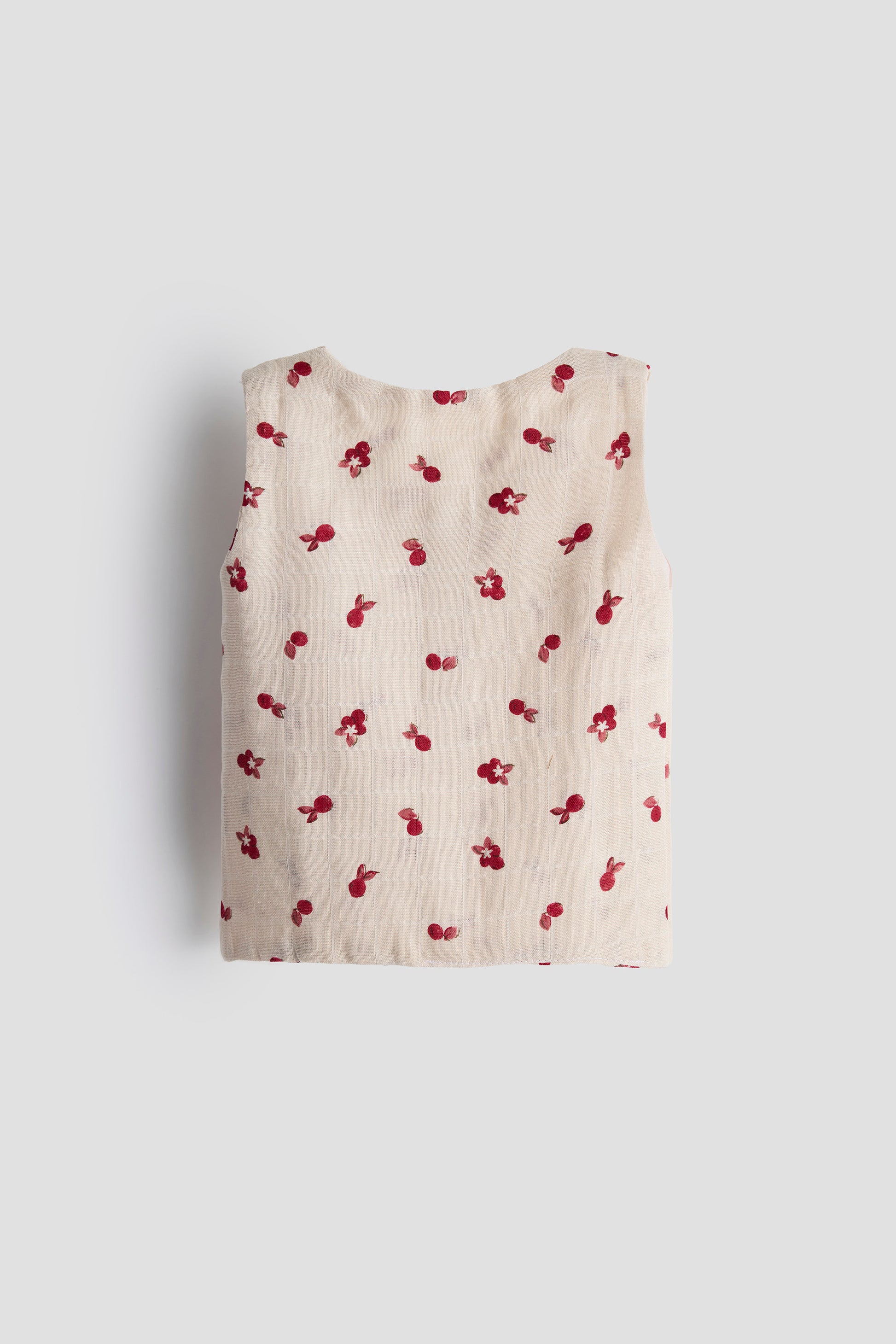 Beige sleeveless top with red cherry pattern on a white background