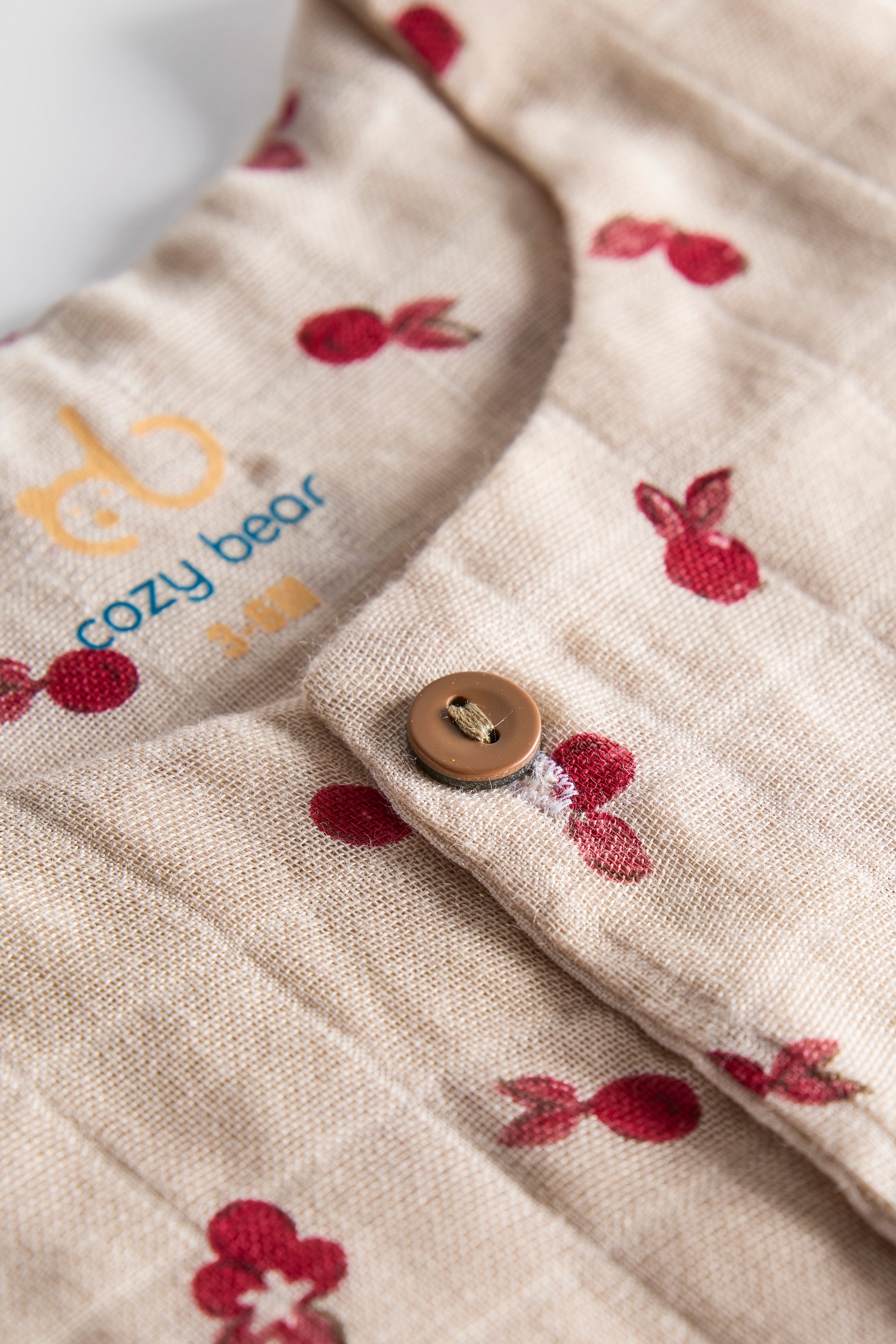 Close-up of a baby outfit with cherry pattern and 'cozy bear' branding.