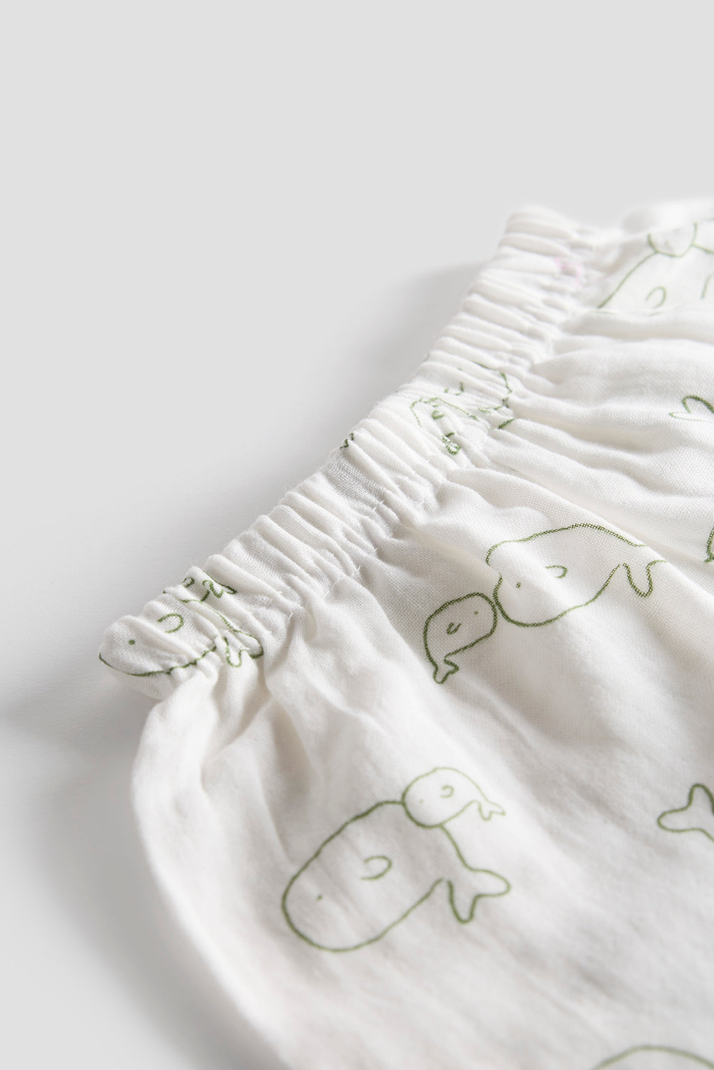 White fabric with green whale patterns on a light gray background