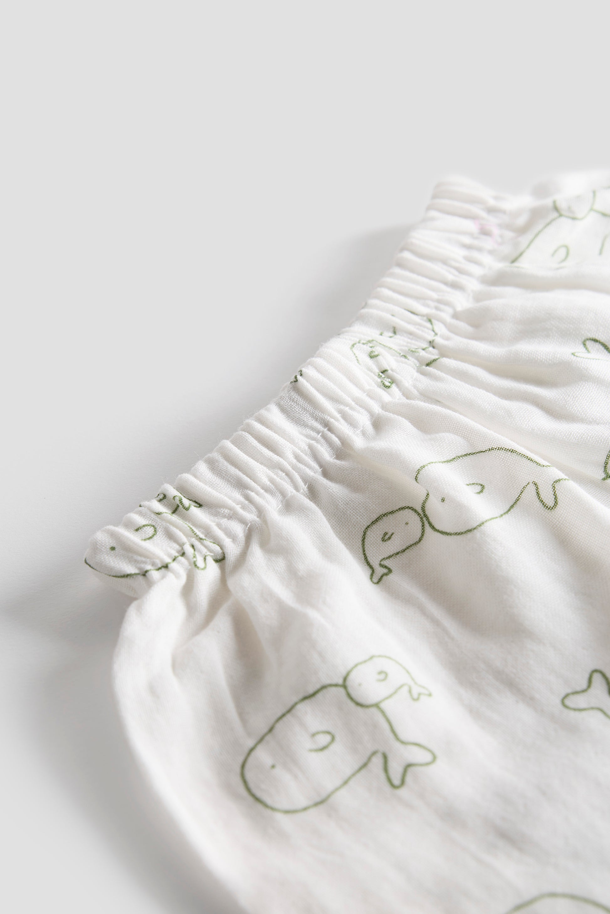 White fabric with green whale patterns on a light gray background